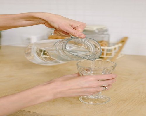 Person pouring fresh water into a glass on a wooden table